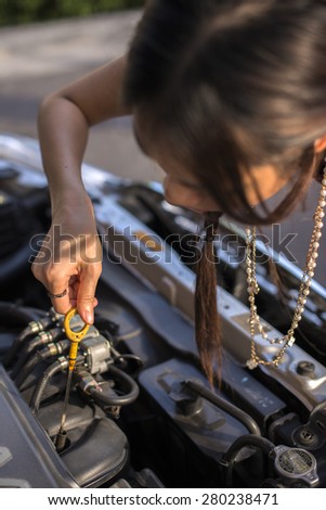 Cute woman driver checking level of oil on a car engine dipstick. Portrait of Asia
