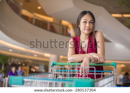 Happy young woman pushing trolley in supermarket. Portrait of Asia