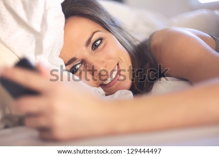 Happy woman lying on bed smiling while reading a text message from someone