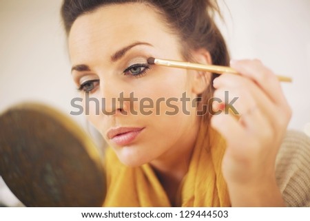 Attractive woman applying makeup while looking at the mirror