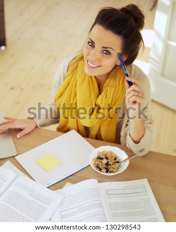 Happy woman holding a pen sitting at home studying her books
