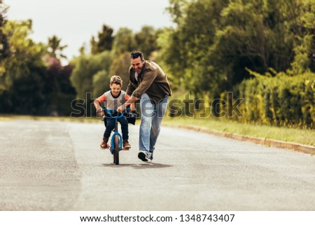 Kid riding a bicycle while his father runs along holding the bicycle. Happy kid having fun learning to riding a bicycle with his father.
