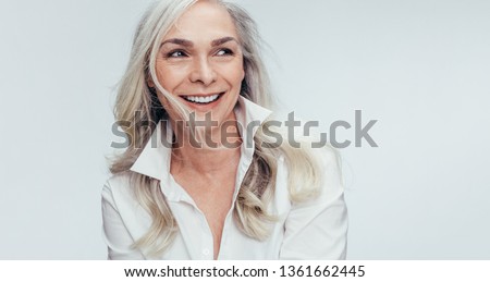 Elegant mid adult woman against white background. Stylish mature woman in white casuals looking away and smiling.