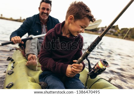 Close up of a kid sitting in a kayak catching fish holding a fishing rod. Happy man rowing a small boat in a lake while his kid tries to catch fish using a fishing rod.