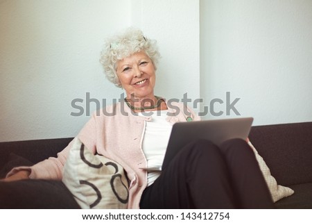 Happy senior woman sitting on the couch at home with laptop