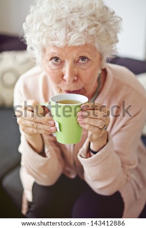 Closeup of a mature lady looking at you while drinking her tea