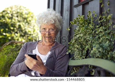 Senior woman using a mobile phone while sitting on bench in her backyard garden