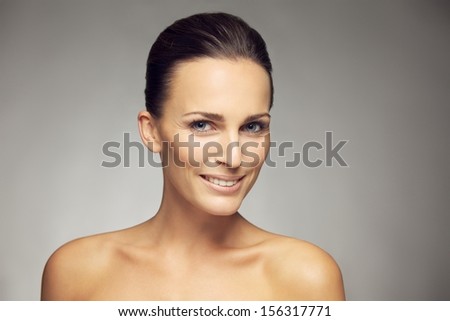 Closeup of a beautiful young woman with perfect healthy skin looking at you smiling  isolated on gray background. Natural Beauty with fresh and clean skin