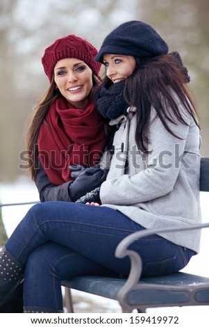 Two happy women sitting on a park bench on a cold winter