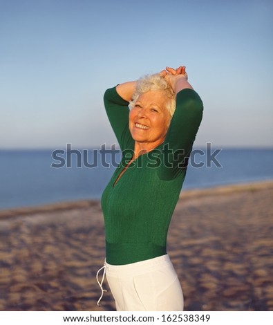 Happy elder woman looking relaxed on the beach with her hands on her head. Active senior female on the beach relaxing