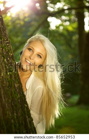 Natural young beauty hiding behind a tree. Sun is shining.