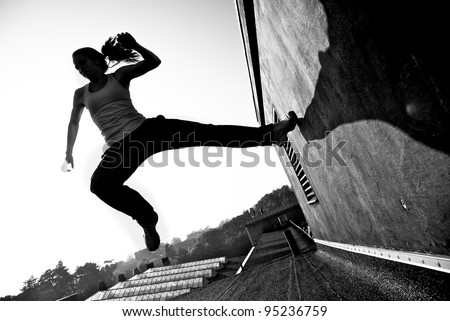 Monochrome image of a female traceur using momentume and speed to propel herself through the air between two buildings while participating in parkour.