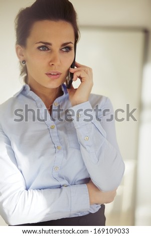 Elegant young woman talking business on the phone. Beautiful caucasian female in blue shirt looking away using phone.