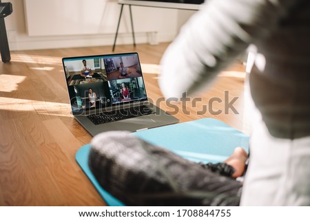 View of a woman conducting virtual fitness class with group of people at home on a video conference. Fitness instructor taking online yoga classes over a video call in laptop.