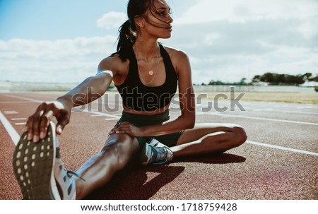 Athlete doing stretching exercises on running track. Woman runner stretching leg muscles by touching his shoes and looking away.