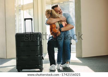 Girl greets her dad at the door when he arrives back from a trip. Daughter hugging her father just arrived from a business trip with a travel case.