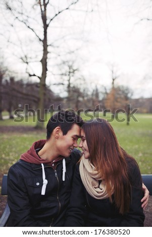 Teenage couple sitting on a bench and enjoying a day in the park. Beautiful young couple in park. Mixed race male and female model in love with copy space.