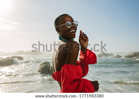 Attractive woman in red dress dancing on the beach. African woman wearing red sundress and sunglasses having fun on the beach.