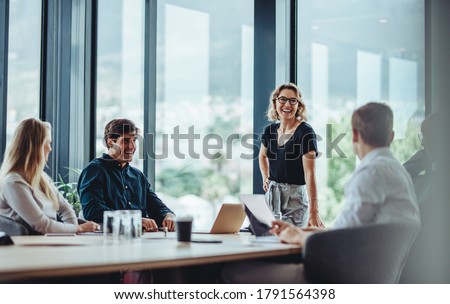 Photo of Office colleagues having casual discussion during meeting in conference room. Group of men and women sitting in conference room and smiling.