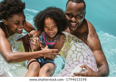 Man and woman playing with their daughter on inflatable ring in swimming pool. Family of three enjoying summer holidays in swimming pool.