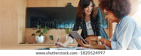 Photo of Shot of two businesswoman working together on digital tablet. Creative female executives meeting in an office using tablet pc and smiling.