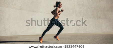 Healthy young woman running in morning. Fitness model exercising in morning outdoors. Panoramic side shot of fit woman.