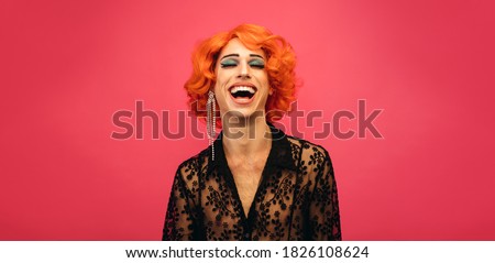 Portrait of drag queen laughing on red background. Gender fluid male dressed as female laughing.