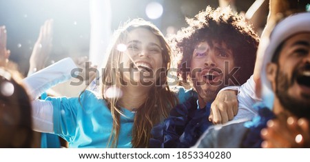 Cheerful couple cheering at a live soccer match. Group of people in the stadium cheering argentina football team.