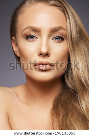 Close up portrait of pretty blond woman on grey background. Perfect face and makeup. Looking at camera.