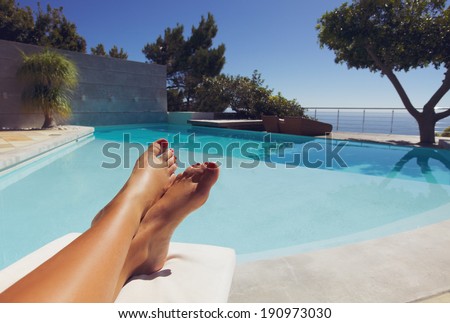 Bare feet of young lady lying on deck chair sunbathing by the swimming pool.
