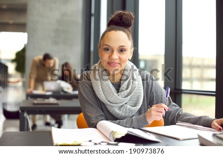 Confident young female student studying. Woman sitting at desk with books.