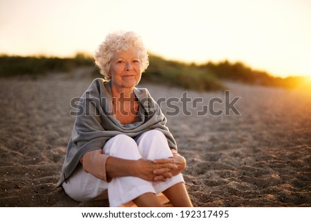 Portrait of happy old woman sitting on the beach. Retired caucasian lady relaxing outdoors