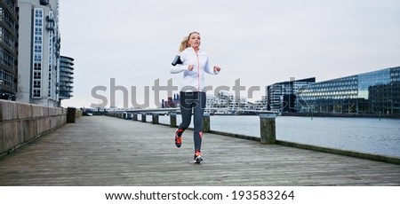 Young female athlete running on boardwalk along the river. Fit young woman jogging along the waterfront.
