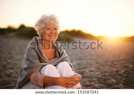 Portrait of smiling old woman sitting on the beach. Senior caucasian female relaxing outdoors
