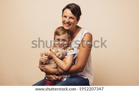 Portrait of carrying mother with her son after receiving a vaccine on arm. Mother and son with bandage on arm after getting immunity vaccine.