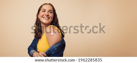 Attractive woman showing her arm after receiving a vaccine and looking away on brown background. Woman looking happy after getting immunization vaccine.
