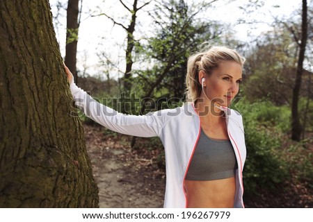 Fit female taking a break after running on forest trail. Pretty young woman wearing headphones listing to music and looking away.