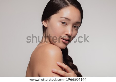 Attractive young asian woman with glowing skin. Korean female with beautiful skin looking at camera against beige background.