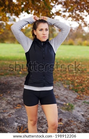 Portrait of attractive young woman preparing for run in park. Fit and healthy caucasian female athlete in sports clothing looking away. Beautiful female runner in autumn park.