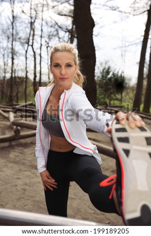 Young caucasian female athlete stretching her muscles before a training session in forest. Fit young woman exercising outdoors.