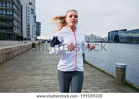 Fit young woman running on the boardwalk along river. Caucasian female athlete training outdoors by the waterfront.