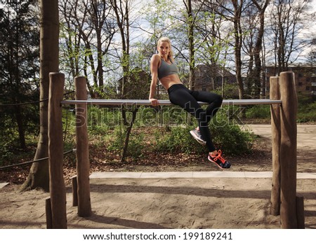 Fit young female sitting on parallel bars. Woman taking rest after triceps dips exercise at park.