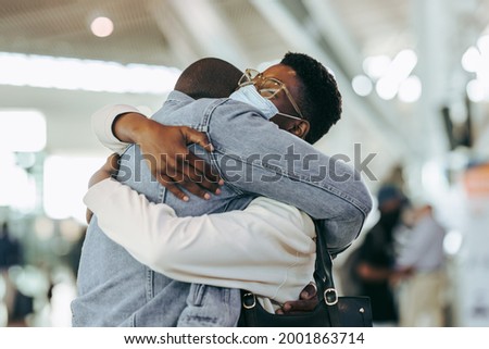 Man hugging woman during pandemic at airport terminal. African couple reuniting at airport arrivals.