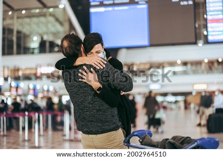 Excited woman meeting husband during pandemic at airport arrival gate. Man giving warm hug to his wife on arrival at airport in pandemic.