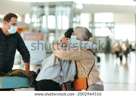 Senior woman welcoming her daughter arriving at airport after pandemic. Woman greeting her mother at airport arrival while her husband looks.
