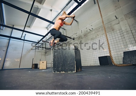 Low angle view of young female athlete box jumping at a crossfit gym. Fit woman is performing box jumps at gym.