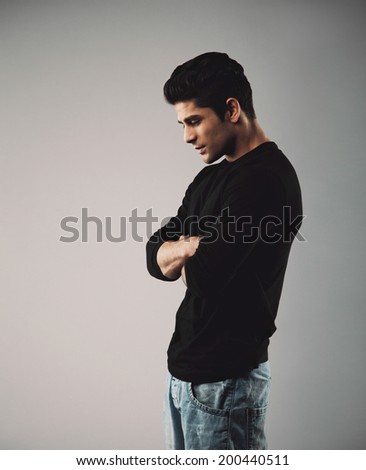 Young man in casuals standing with arms crossed looking down. Male model on grey background.