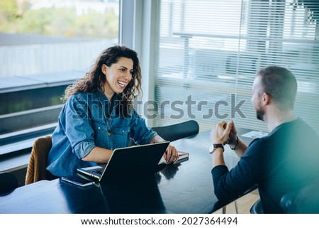 Smiling businesswoman taking interview of a job applicant. Friendly recruitment manager interviewing young man in office boardroom. Foto d'archivio © 