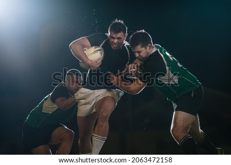 Rugby player in possession of the ball and attempting to advance. Rugby players blocking and tackling opponent player to get the ball.