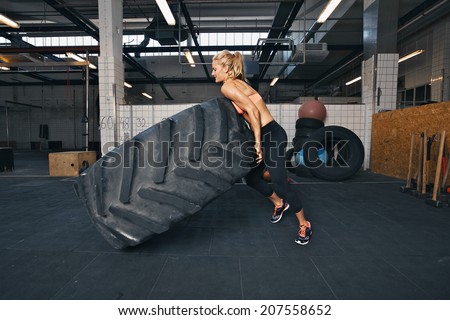 Fit female athlete flipping a huge tire. Muscular young woman doing crossfit exercise at gym.